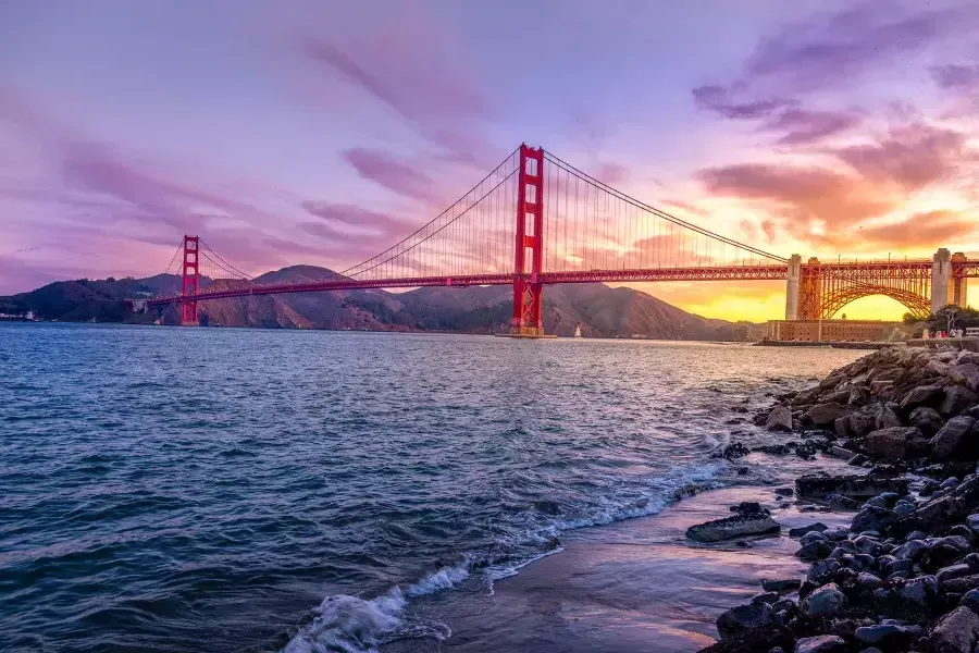 Il Golden Gate Bridge al tramonto con un cielo multicolore e la Baia di San Francisco in primo piano.